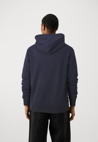 Marineblå hættetrøje med snoretræk, ribbede manchetter og kant, samt en afslappet pasform. Stoffet fremstår blødt med minimal struktur.