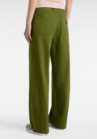 Gröna vida byxor i ett texturerat tyg, med en knappficka bak och i kombination med rutiga skosnören.