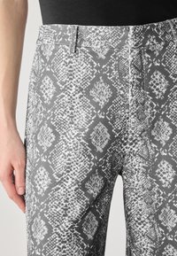Grijze gestreepte broek met een slangenhuid ontwerp, voorzien van diamantvormen en variërende texturen. Gemaakt van een gladde stof met een op maat gemaakte taille.