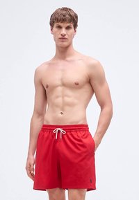 Short de baie roșii cu talie elastică și șnur, având buzunare laterale și un mic logo pe partea inferioară a piciorului.