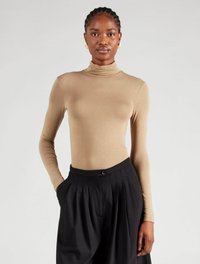 Beige Rollkragenoberteil mit langen Ärmeln, kombiniert mit hochtaillierten schwarzen, plissierten Hosen. Glatte Textur, figurbetontes Design und Knopfverschlussdetail.