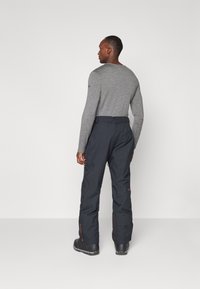 Gray long-sleeve shirt paired with black waterproof snow pants, featuring contrasting orange zippers and a relaxed fit. Low-profile boots.