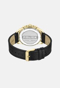 Cassa dell'orologio in acciaio inossidabile dorato con quadrante rotondo bianco. Cinturino in pelle nera con superficie texturizzata e fibbia dorata, impresso con la scritta "POLICE."