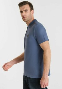 Polo shirt bleu en tissu texturé, à manches courtes et avec un col à trois boutons. Présente un petit logo sur la poitrine.