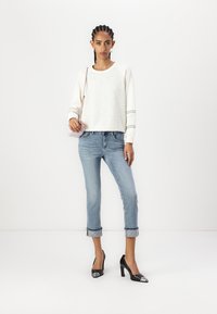 Sudadera blanca texturizada con rayas negras, jeans cortos de color azul claro y tacones negros de punta. Sosteniendo un pequeño bolso rosa.