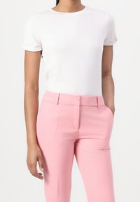 T-shirt blanc à col rond avec des manches retroussées, associé à un pantalon rose taille haute, ajusté, avec des poches avant et une finition lisse.