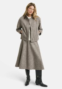 Veste en mélange de laine marron avec fermeture éclair et poches latérales, assortie d'une longue jupe évasée. Bottes en cuir noires jusqu'aux genoux.