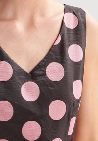 Vestido negro con escote en V, que presenta grandes lunares zigzagueantes en rosa tejido. La tela es suave con un ligero brillo y acentos texturizados.