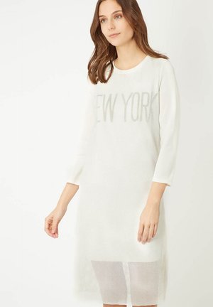 Vestido blanco de manga tres cuartos con textura de malla y "NEW YORK" impreso en letras reflectantes. Sección inferior transparente hasta la rodilla.