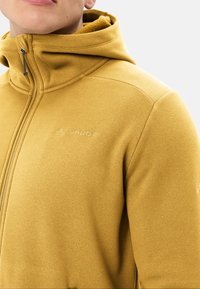 Giacca in pile gialla con cappuccio, dotata di zip completa, texture morbida e dettagli del logo discreti sul petto.