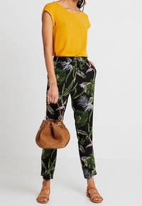 Žlutý krátký rukáv spárovaný s černými kalhotami s vzorem zelených listů. Hnědá kabela typu bucket, ploché sandály a ležérní outfit.