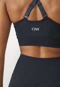 Sujeción deportiva de color azul oscuro con textura acanalada, tirantes ajustables y logo de ICIW. Cuenta con un diseño de soporte y una construcción sin costuras en la parte posterior.