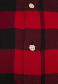 Tessuto a scacchi rosso e nero con bottoni color crema cuciti su un ripiego cucito.