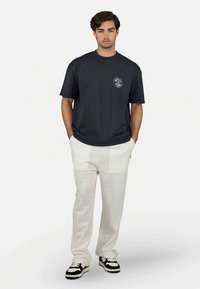 Tricou din bumbac de culoare bleu închis, cu mâneci scurte, având un grafic pe față. Asortat cu pantaloni din in alba și adidași alb-negru.