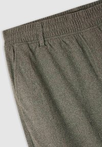 Szare spodnie z tkaniny tweedowej z elastycznym paskiem, dziurkami na pasek i detalem bocznej kieszeni na jednolitym tle.