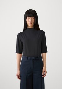 Top nero a maniche corte con collo alto e discreto dettaglio del logo abbinato a pantaloni a gamba larga blu navy con vita con cintura. Texture liscia.