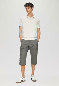 Light beige polo shirt with a collar, paired with knee-length grey cargo shorts featuring side pockets and a relaxed fit. White sneakers.
