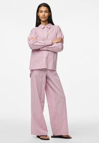 Gestreept pyjamastel in roze en wit. Het bovenstuk heeft een kraag en een zak; de broek is wijd en heeft een relaxte pasvorm. Licht, zacht materiaal.