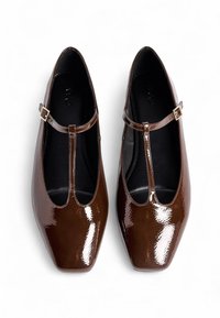 Bailarinas de charol marrón con un diseño de tira en T. Presentan una punta cuadrada, una hebilla dorada minimalista y una textura suave.