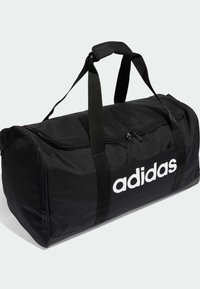 Schwarze Sporttasche aus strapazierfähigem Stoff, mit einem Reißverschluss oben, zwei stabilen Griffen und großem weißem Logo an der Seite.