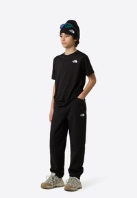 Μαύρο βαμβακερό t-shirt και παντελόνια από τη The North Face, με λογότυπα. Αξεσουάρ περιλαμβάνουν μαύρο σκουφάκι και πολύχρωμα γυαλιά ηλίου.