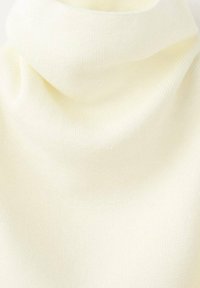 Golf w kolorze kremowym, wykonany z miękkiej, prążkowanej tkaniny o luźnym kroju. Materiał wydaje się lekki i gładki, odpowiedni do noszenia warstwowego.