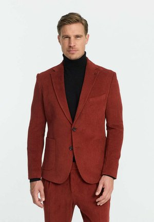 Rotes Cordhosenblazer mit tailliertem Schnitt, zwei vorderen Taschen, Reverskragen und einer Ein-Knopf-Verschluss. Über einem schwarzen Rollkragenpullover getragen.