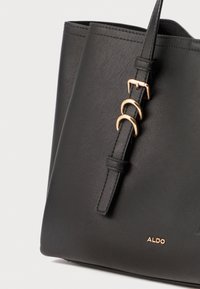 Schwarze Leder-Tote-Bag mit strukturierter Form, verstellbarem Tragegurt und goldfarbenen Hardware-Details sowie einem dezenten Logo am Boden.