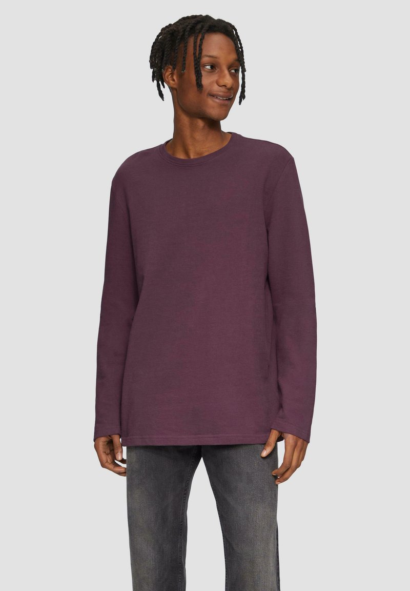 Langes lila T-Shirt mit Rundhalsausschnitt, aus weichem Stoff, kombiniert mit dunklen Jeans. Angenehme Textur, lässige Passform.