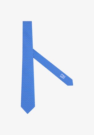 Cravatta blu con un motivo ripetuto di piccoli fenicotteri bianchi e un'etichetta visibile sul lato inferiore vicino all'estremità appuntita.