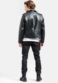 Schwarze Leder-Motorradjacke mit Schulterklappen, tailliertem Schnitt und glatter Textur. Kombiniert mit schwarzen Jeans und robusten schwarzen Stiefeln.
