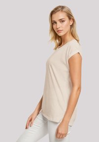 Beige cotton t-shirt with short rolled sleeves, round neckline, and a relaxed fit. Paired with white jeans. Smooth texture.