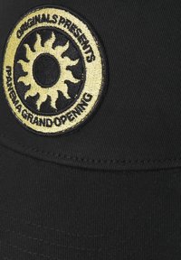 Zwarte pet van textuurstof met een ronde geborduurde patch met een gele zonontwerp en de tekst "Originals Presents Panena Grand Opening."