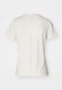 Camiseta crema de manga corta, con cuello redondo, hecha de algodón suave. La parte trasera presenta una textura simple y lisa sin adornos.