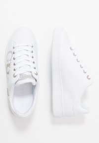 Baskets blanches avec une tige en synthétique lisse, œillets en argent et détail de logo. Présente une semelle en caoutchouc texturée et un système de laçage.