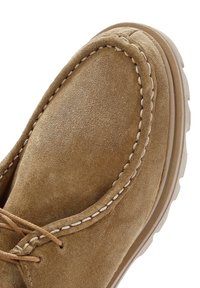 Chaussure en daim marron avec un bout arrondi, une couture blanche contrastante le long des bords, et une semelle en caoutchouc durable. Les lacets sont noués à l'avant.