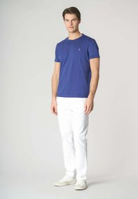 T-shirt in cotone blu con maniche corte, scollo rotondo, caratterizzato da un logo sottile. Abbinato a pantaloni bianchi a gamba dritta e sneaker chiare.