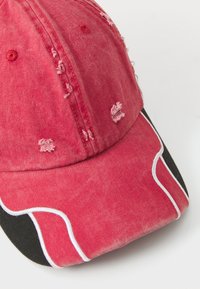 Rød denim baseballcaps med slitt detaljer, svart skygge og hvite sømmer langs sidene. Rund krone design.