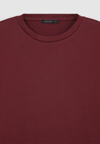 T-shirt bordeaux a manica corta con scollatura rotonda realizzato in morbido tessuto di cotone, con un'etichetta che indica la taglia L e una superficie liscia, non testurizzata.