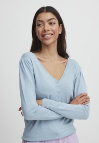 Pull-over léger bleu clair en V avec un devant à boutons, des manches longues avec des épaules froncées et un ourlet côtelé. Texture douce.