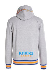 Felpa grigia con cappuccio caratterizzata da un logo "Champion" colorato sul cappuccio e "KNICKS GAMING" in blu e arancione sul retro, con polsini a righe.