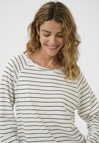 Kreemikas triiksärk pikkade varrukatega, millel on tumesinised horisontaalsed triibud, lai kaelus ja raglaanvarrukad. Pehme kangas ja mugav lõige.