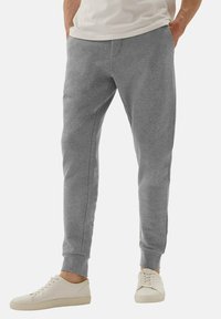 Jasnoszare dresy bawełniane z zwężanymi nogawkami, ściągaczami na mankietach i kieszeniami bocznymi, noszone z beżowymi sneakersami. Prosty i swobodny design.