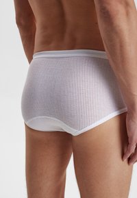 Hvide mesh shorts med en tætsiddende pasform, struktureret overflade med små perforeringer og en solid linning. Bagfra vises en buet skæring.