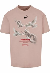 Lyserød bomulds t-shirt med et grafisk motiv af duer og kæder, med ordet "FRIHED" trykt i fed rød tekst. Rund halsudskæring.