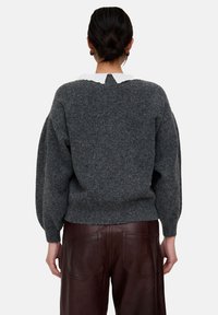 Grauer Wollpullover mit weiter, locker sitzender Passform und weißem Kragen. Der Rücken hat eine kleine Öffnung, kombiniert mit braunen Lederhosen.
