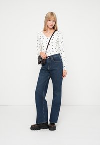 Valge pika varrukaga särk musta lillemustriga, kombineeritud kõrge vöökohaga tumedate siniste teksade ja tükkmustade saabastega. Must õlakott.