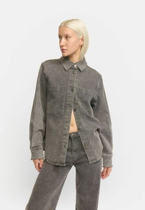 Grijze denim shirt met een knoopsluiting aan de voorkant, twee borstzakken en een kraag. De stof heeft een zachte textuur met een licht vervaagd uiterlijk.
