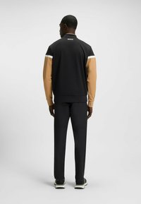 Black jacket with beige sleeves, featuring a white stripe on shoulders and the logo "BOSS" at the back. Paired with matching black pants.