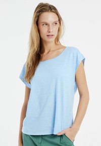 Lichtblauw, kort-sleeve top met een ontspannen pasvorm en brede halslijn. Gemaakt van een zachte, lichtgewicht stof met een gladde textuur.